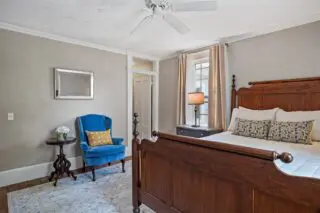 Cozy bedroom with wooden bed, blue armchair, and neutral decor.