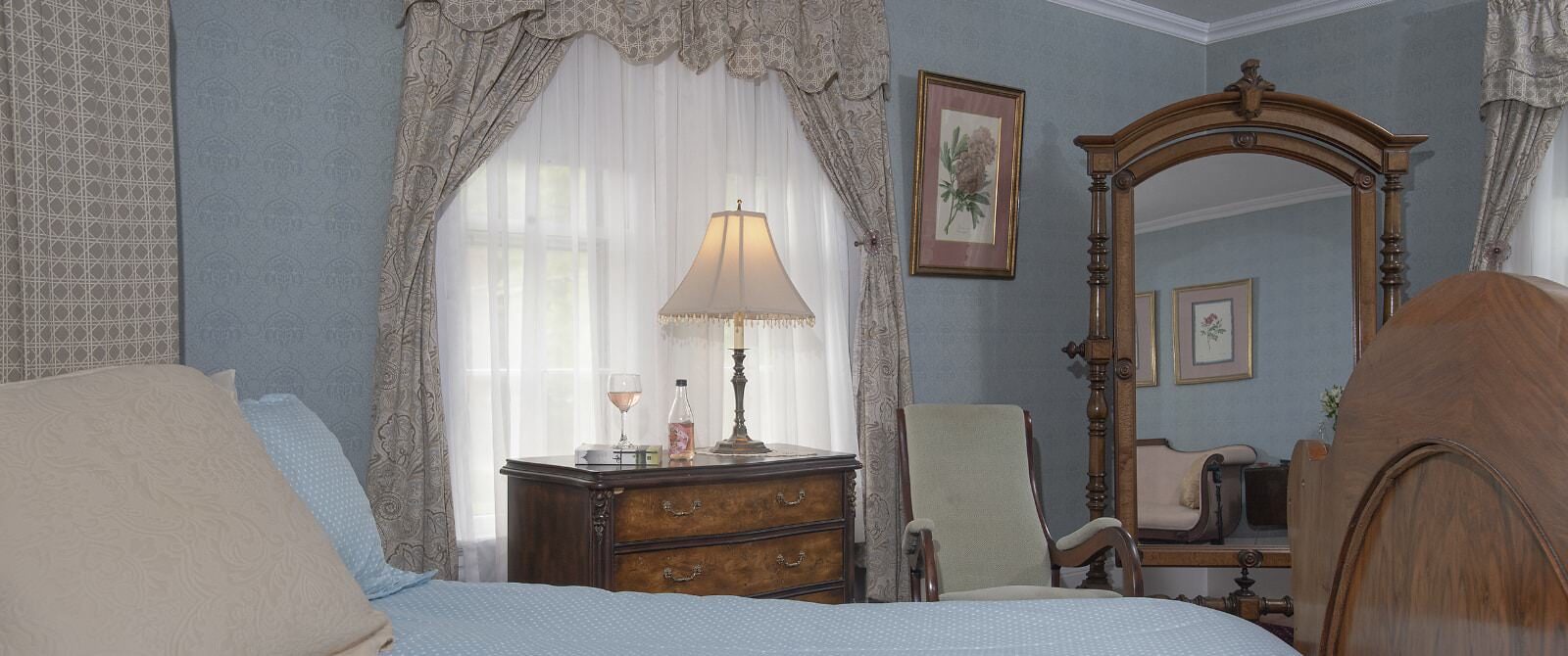 Bedroom with light blue wallpaper, carpeting, antique canopy bed, light blue bedding, and antique dark wooden dresser and floor mirror