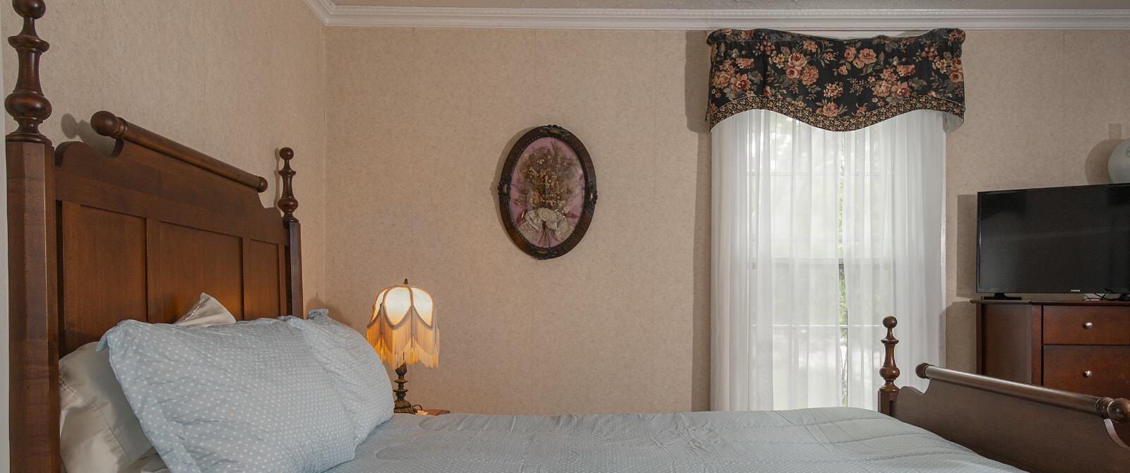 Bedroom with light peach wallpaper, antique wooden headboard, light blue bedding, and dark wooden dresser