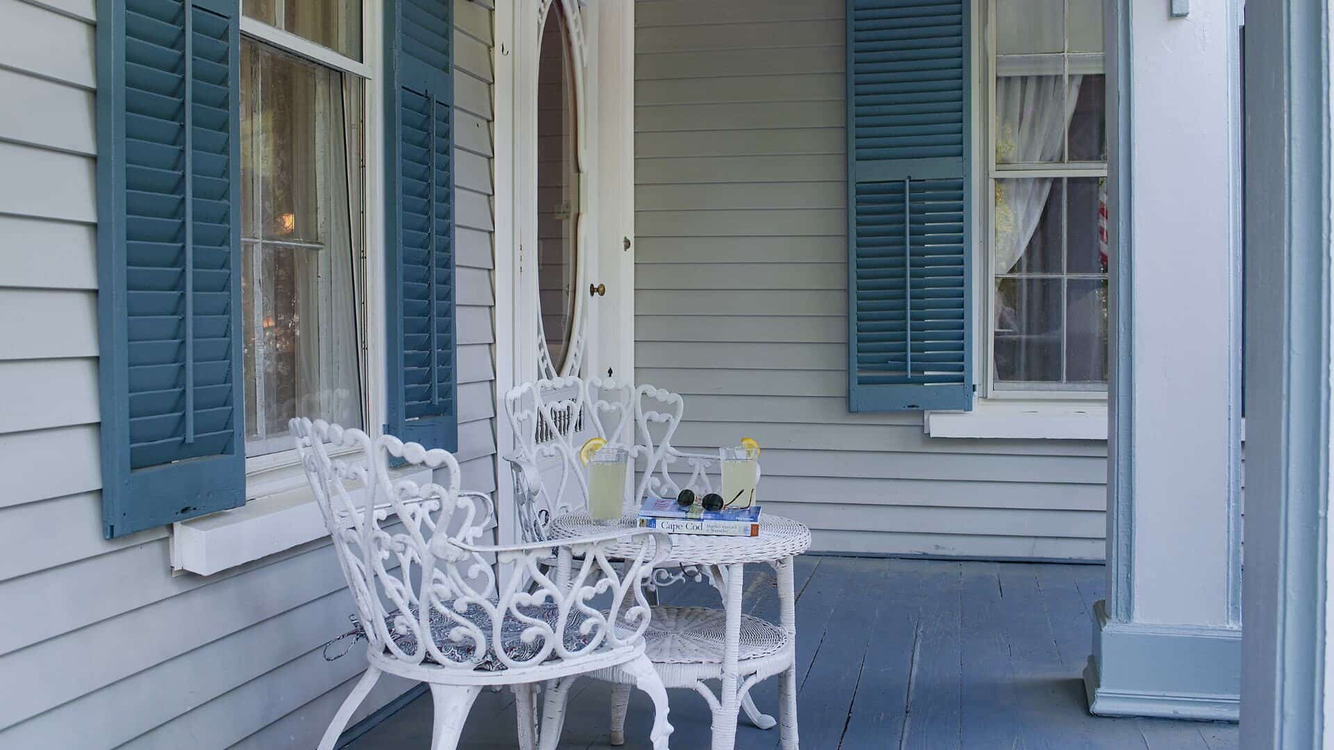 Exterior view of property's front porch with white wrought iron chairs and white wicker small table
