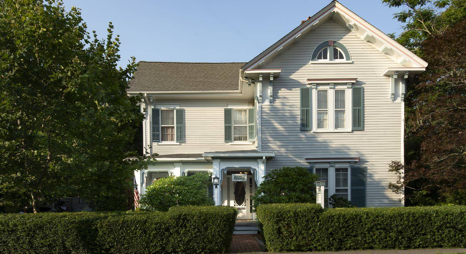 Exterior view of property painted light blue with white trim surrounded by green bushes and shrubs